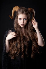Portrait of an attractive demon woman with horns and curly hair, studio shot for Halloween
