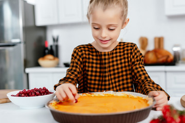 adorable little child decorating thanksgiving pumpkin pie with berries