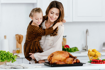 beautiful young mother and daughter embracing while cooking thanksgiving turkey together