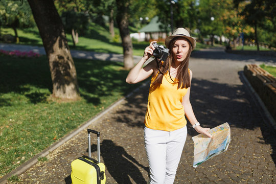 Young traveler tourist woman in hat with suitcase, city map take pictures on retro vintage photo camera in city outdoor. Girl traveling abroad to travel on weekend getaway. Tourism journey lifestyle.