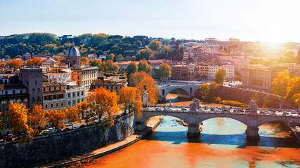Fototapeta na wymiar Skyline with bridge Ponte Vittorio Emanuele II and classic architecture in Rome, Vatican City scenery over Tiber river. Autumn view with red foliage.
