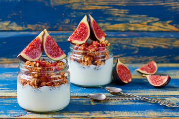 Chia milk pudding with granola and fresh figs in the glass jars on the blue wooden kitchen table. Detox superfoods breakfast or healthy dessert. Side view