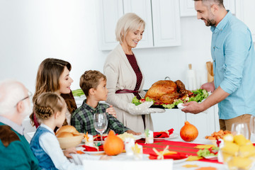 senior woman and adult man carrying baked turkey for thanksgiving dinner with family at home
