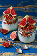 Detox superfoods breakfast or healthy dessert - chia milk pudding with granola and fresh figs in the glass jars on the blue wooden background. Close up view
