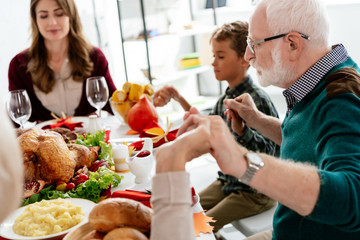 happy family praying at served table with turkey before holiday dinner on thanksgiving