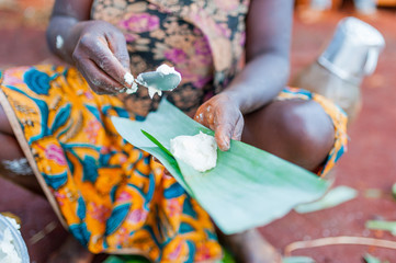 close up of african woman hands filling plantain leaves  with manioc to make traditonal cameroonian baton de manioc in village © davide bonaldo