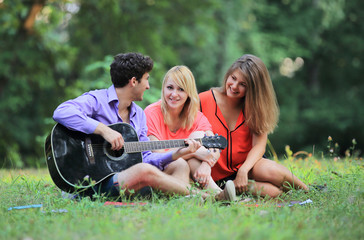 Fototapeta na wymiar group of students with a guitar relax sitting on the grass in the city Park