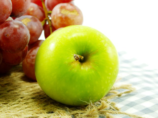 green apple and red grapes on tablecloth