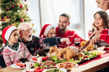 senior woman cutting turkey for christmas dinner with happy family at home