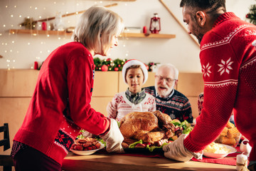 partial view of adult man with senior woman carrying turkey for holiday dinner with family at home