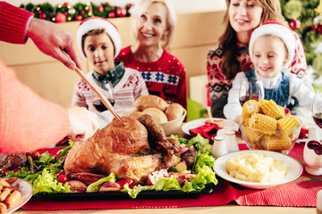 cropped image of man cutting holiday turkey for christmas dinner with happy family at table