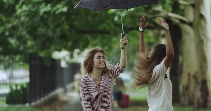 Quickly video moving , two young women jumping under the umbrella on rain day in the middle of street. slow motions