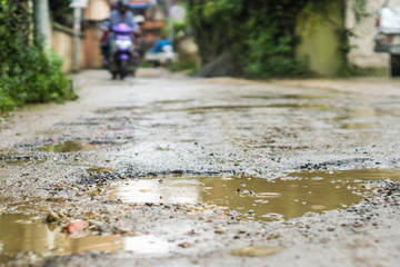 Rain falls in mud puddles in rough road, motorcycle blurred in background