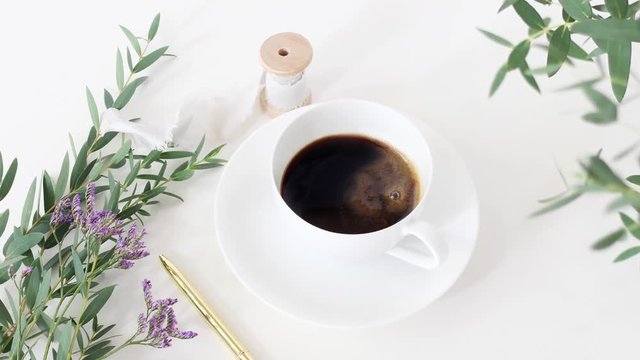 Cinemagraph. Cup of coffee, wedding bouquet, silk ribbon and golden pen on white table background. Eucalyptus branches moving in breeze. Feminine breakfast desktop composition. Top view. Loopable.
