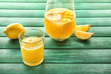 Glass and jug of fresh lemon juice on color wooden table