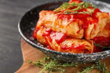 Plate with stuffed cabbage leaves in tomato sauce on wooden board, closeup