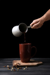 Woman pouring hot chocolate from cezve into cup on wooden table