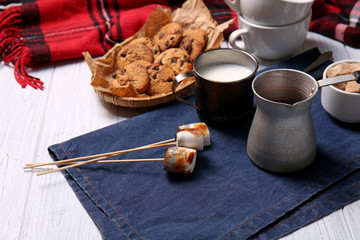 Cezve of hot chocolate with milk and sweets on white wooden table