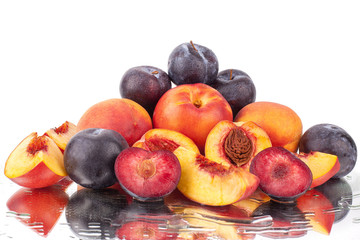 A lot of bright fruits, whole and cut peaches and plums on a mirror white background in water drops isolated