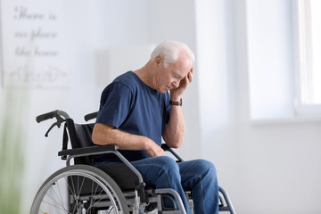 Fototapeta na wymiar Disabled senior man in wheelchair suffering from headache at home
