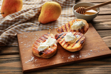 Halves of tasty grilled pears with ice cream on wooden board
