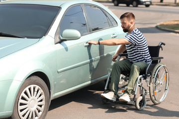Naklejka na ściany i meble Man in wheelchair trying to open his car