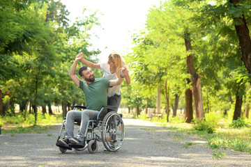 Man in wheelchair with beautiful woman dancing outdoors