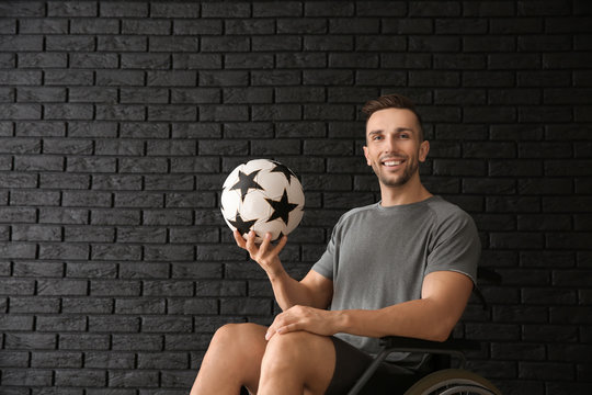 Young Man With Ball Sitting In Wheelchair Against Dark Brick Wall