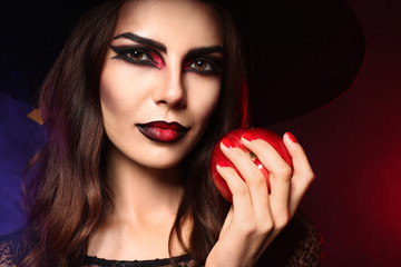 Beautiful woman dressed as witch for Halloween with apple on dark color background