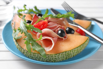 Plate with delicious melon and prosciutto on white wooden table, closeup