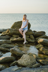 young attractive woman sits on rocks in the sea