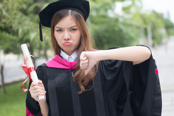 stress, frustrated graduated woman university student points thumb down; portrait of negative, angry, upset woman student graduation with bad thumb down gesture; asian 20s young adult woman model