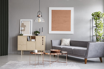 Modern couch and copper tables in a grey living room interior with a painting. Real photo