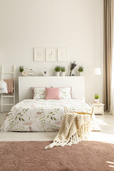 Blanket and pillows on bed with plants on headboard in pink and white bedroom interior. Real photo