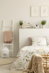 Ladder with pink blanket next to bed in feminine bedroom interior with lavender flowers and posters. Real photo