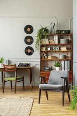 Grey wooden armchair in retro home office interior with chair at desk and vinyl on the wall. Real photo