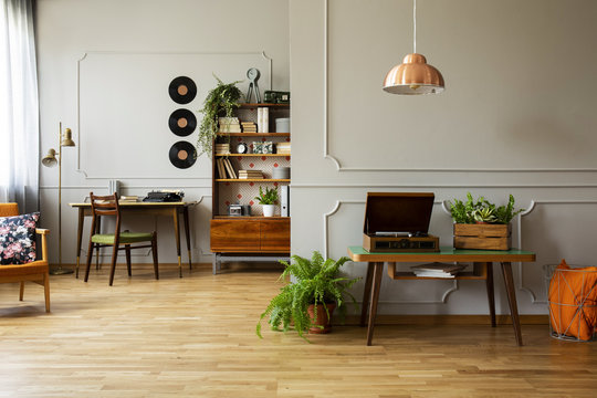 Record player and plant on wooden table in grey apartment interior with lamp and vinyl. Real photo