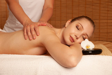 Beautiful young woman having a massage treatment in spa salon - wellness