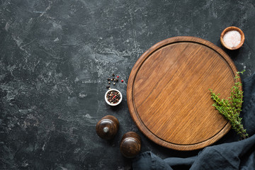 Spices, Herbs, Cutting board for cooking. Round wooden cutting board on black concrete backdrop. Top view with copy space for text. Menu, recipe mock up, banner background