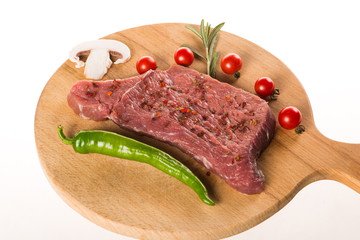 Uncooked steak with spices and vegetables on wooden plate