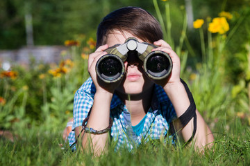 Boy young researcher exploring with binoculars environment in green garden