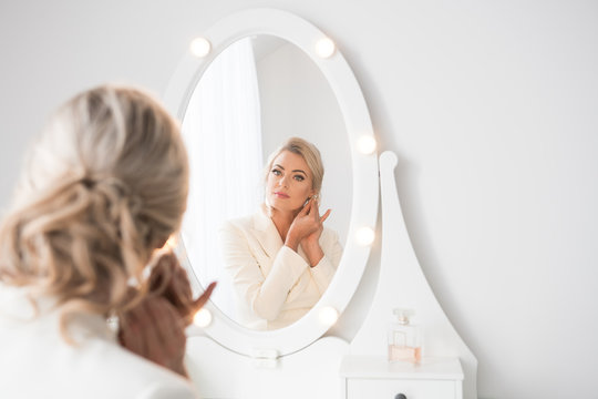 Young woman putting on earrings in front of mirror