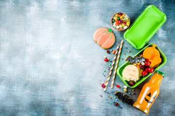 Halloween food, school lunch box with ghost sandwich, carved little pumpkins, cookies, candies and orange juice in funny monster bottle, blue concrete background top view copy space