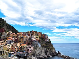 Fototapeta na wymiar Panorama of the city of Manarola in the province of Cinque Terre in Italy, a cozy colorful place, colorful houses are located on a hill above the sea, down the Bay with boats