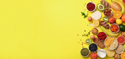 Organic food frame. Banner. Healthy breakfast ingredients. Oat and corn flakes, eggs, nuts, fruits, berries, toast, milk, yogurt, orange, banana, peach on yellow background. Top view, copy space
