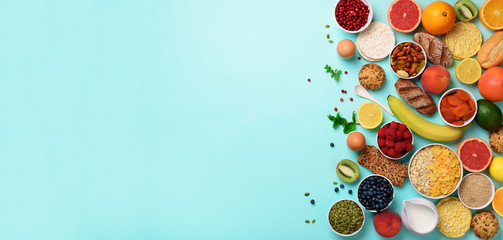 Organic food frame. Banner. Healthy breakfast ingredients. Oat and corn flakes, eggs, nuts, fruits, berries, toast, milk, yogurt, orange, banana, peach on blue background. Top view, copy space