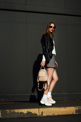Trendy young woman with bag standing next to old building. Street fashion concept, wearing glasses. Girl posing in front of the old wall