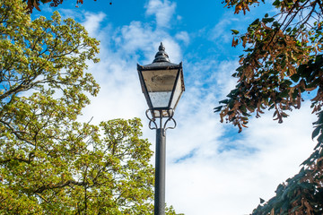 A street light in the style of an old lantern pictured against a blue sky with clouds.