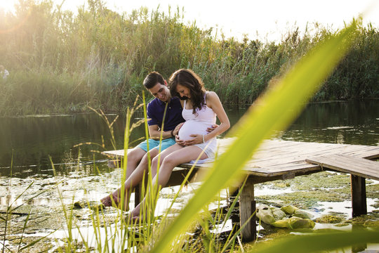 Young pregnant couple sitting on a wood platform over a river