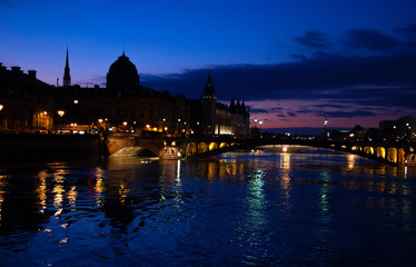 Fototapeta na wymiar Blue hour in Paris. View of Pont au Change bridge and Conciergerie building. Colorful reflection of evening city lights in Seine river water.